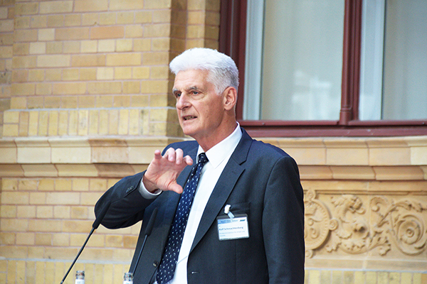 Ein Mann im Anzug redet in ein Mikrofon. Er hat kurze, weiße Haare. Er gestikuliert mit der Hand.