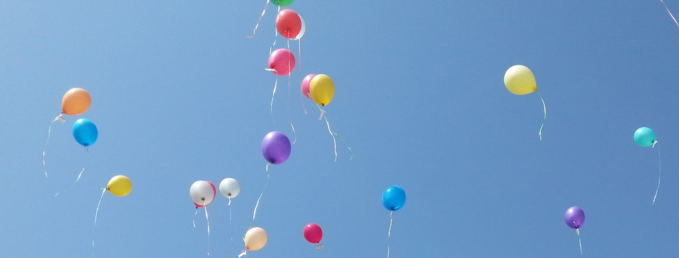 Etwa zwanzig bunte Luftballons schweben verteilt im Himmel.