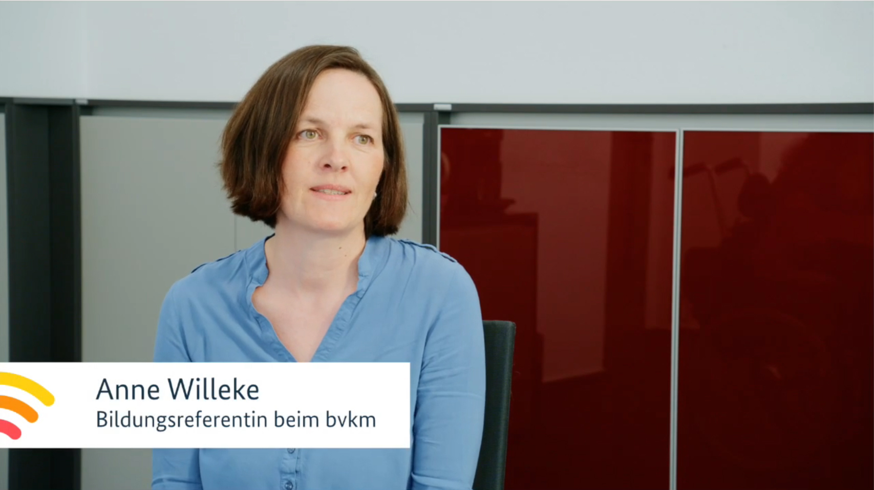 Eine Frau mit schulterlangen, braunen Haaren spricht. Sie trägt eine hellblaue Bluse.