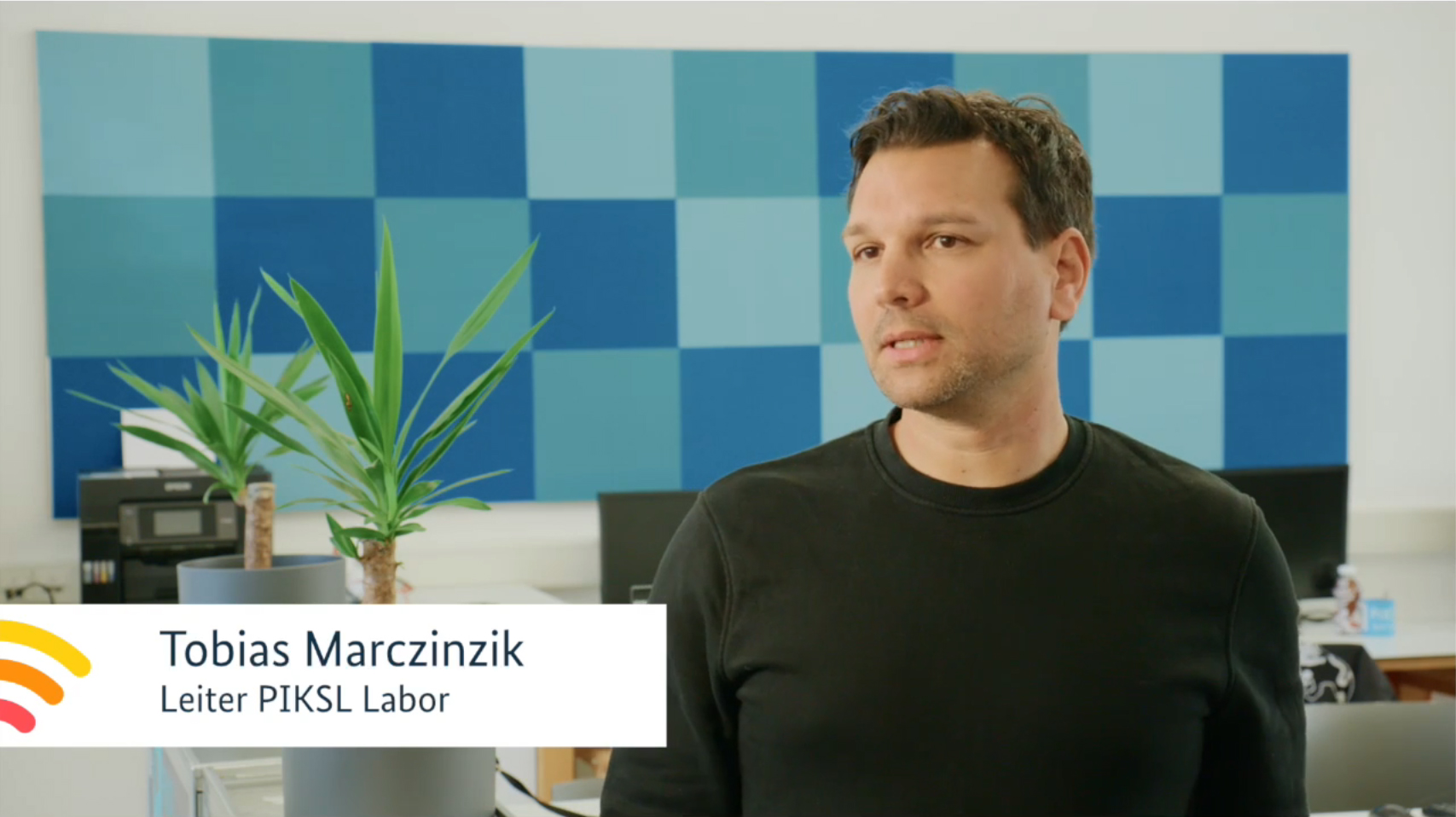 Ein Mann mit kurzen dunklen Haaren spricht. Er trägt ein dunkles Shirt.