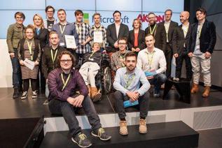 Die Preisträger des "Neue Nähe"-Hackathons von Aktion Mensch und Microsoft auf der Bühne im Microsoft-Gebäude Berlin "Unter den Linden". Im Hintergrund stehen die Moderatoren sowie weitere Mitwirkende der Veranstaltung.