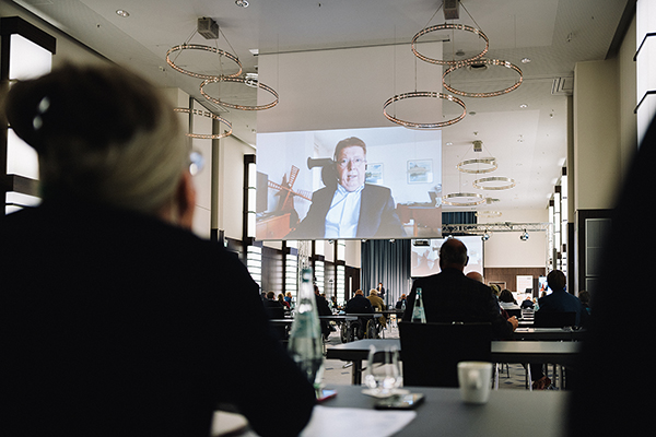 Dr. Volker Sieger auf dem Bildschirm, der im Saal hängt - Foto: Bundesfachstelle Barrierefreiheit/Carsten Beier