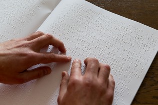 Zwei Hände lesen eine mit Brailleschrift bedruckte Buchseite. Foto: DBSV/A.Friese