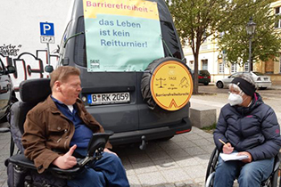 Dr. Sigrid Arnade spricht mit Dr. Volker Sieger. Beide sitzen im Rollstuhl. Sie trägt eine Maske und macht sich Notizen. Foto: Hans-Günter Heiden